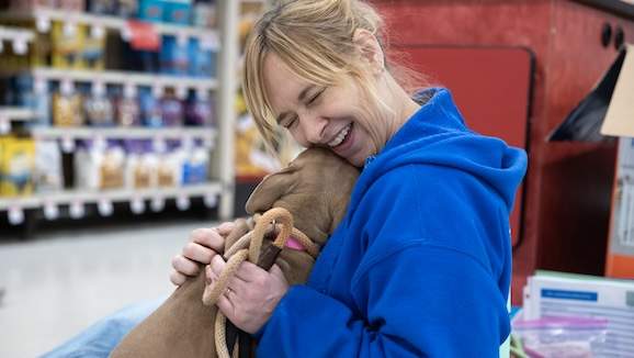 woman with blonde hair laughing as she cuddles a puppy in a PetSmart store