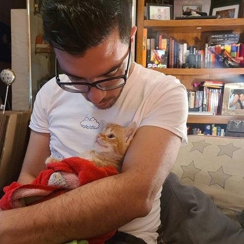 Man looks down at an orange tabby cat he's holding in his arms